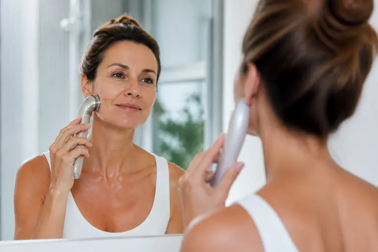 Femme souriante utilisant un appareil d'electrostimulation du visage pour améliorer la fermeté.