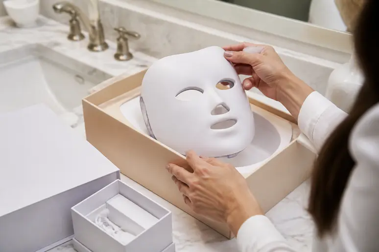Mains déballant un masque LED visage : sécurité et conformité pour la luminotherapie-visage-couleur-signification.